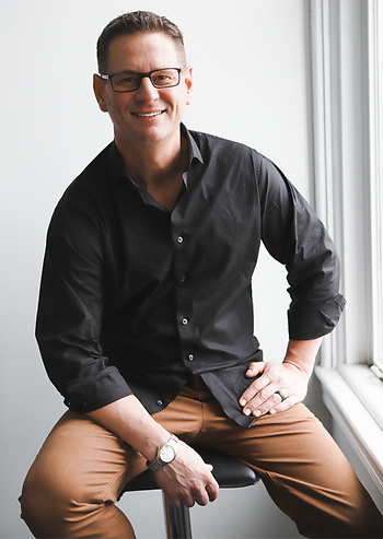 Smiling gentleman in casual wear sitting by a window poses for a portrait 