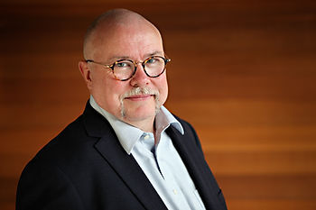 Portrait of a bespectacled man in a suit jacket.